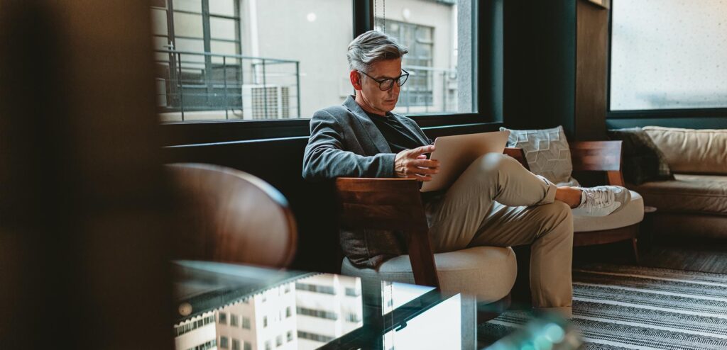 Mature businessman sitting in office lobby with a laptop. Male executive working in office lounge.